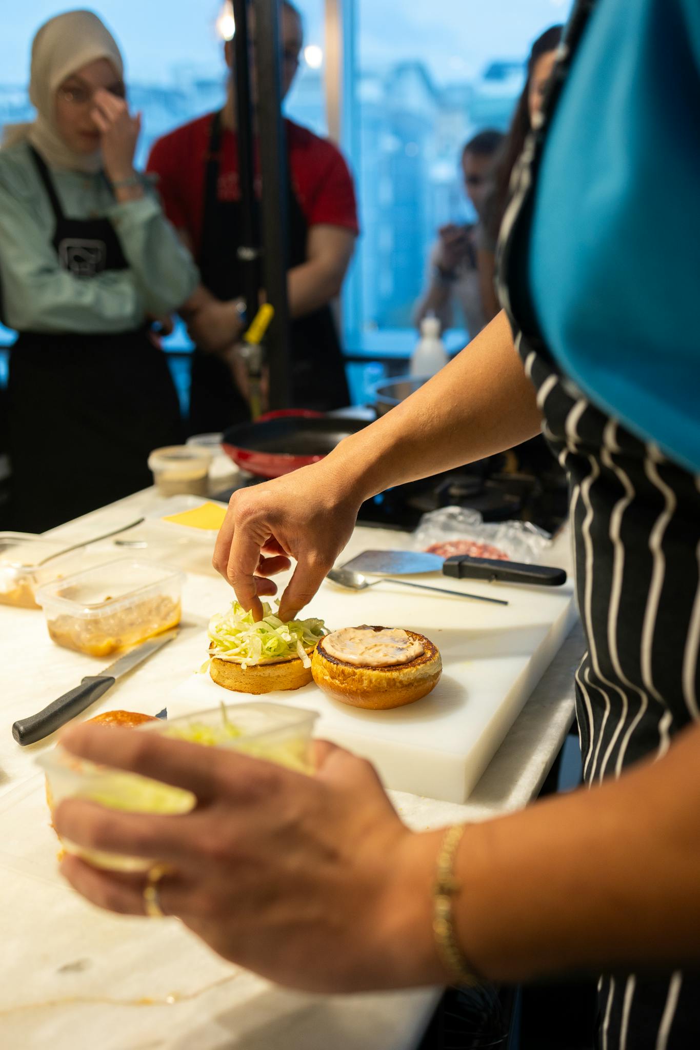 A chef demonstrates gourmet burger assembly during a Samsun cooking class.