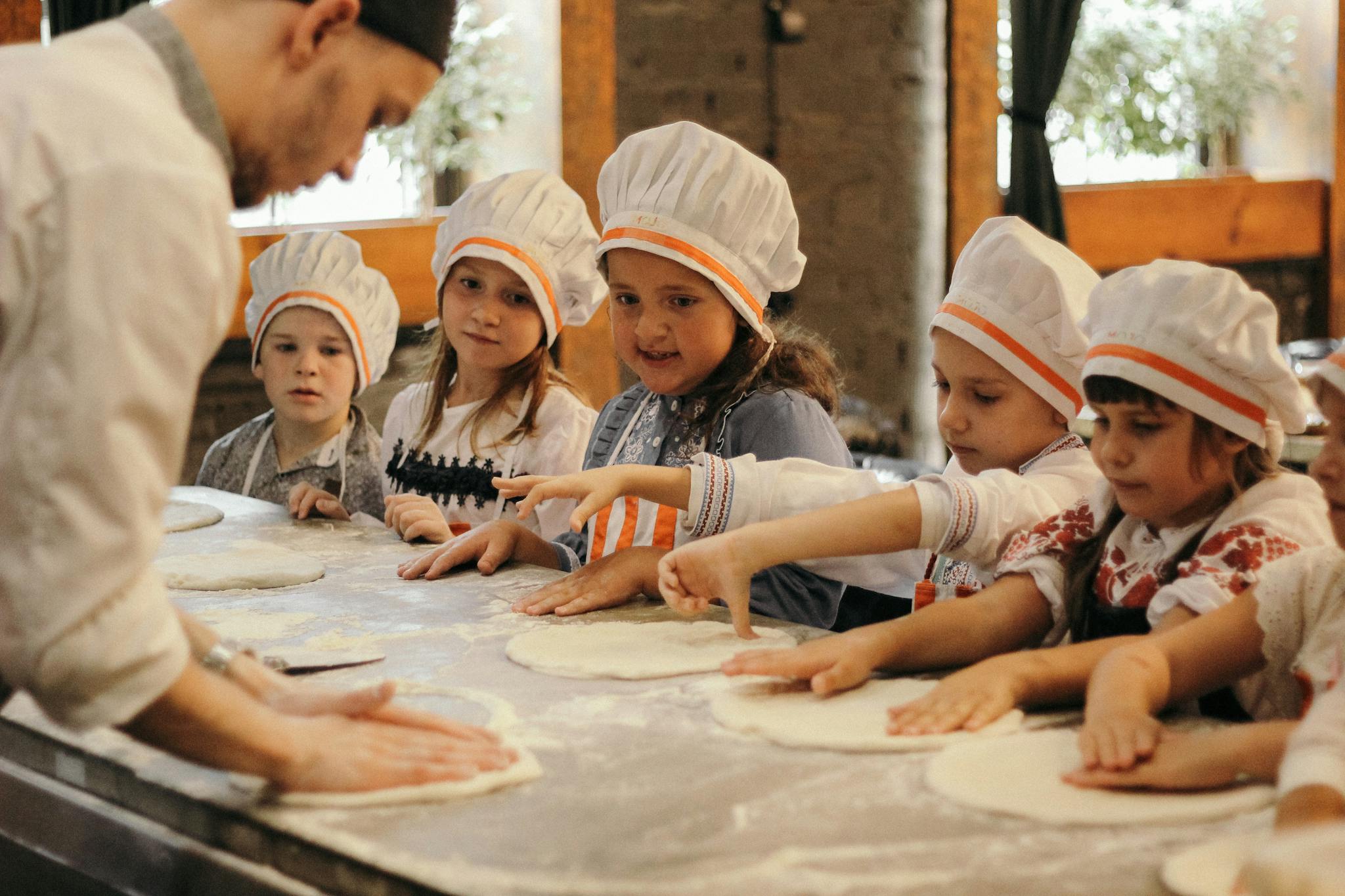 Group of children learning to bake pizza at a restaurant kitchen under a chef's guidance.