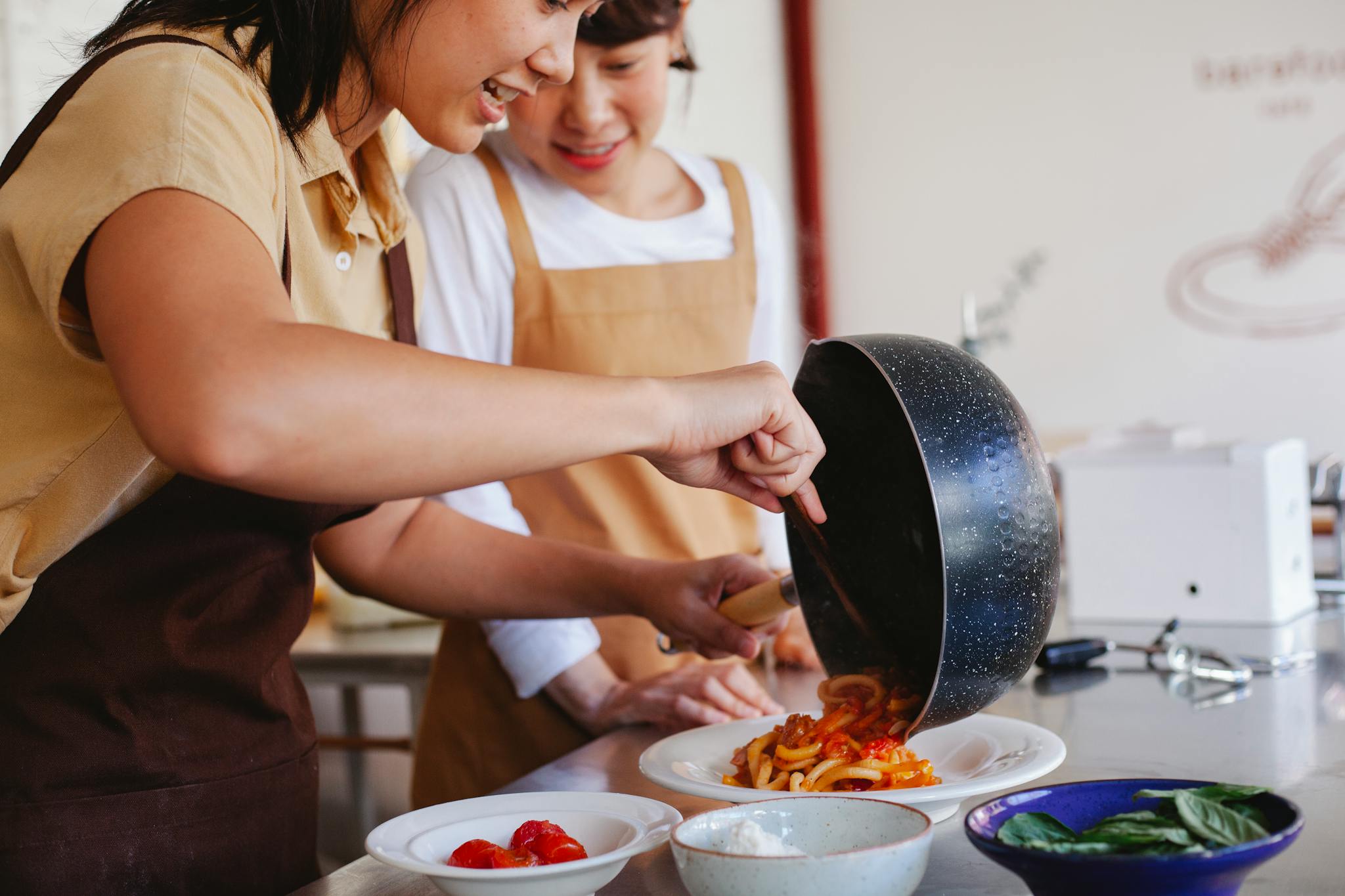 Two women preparing a pasta dish, showcasing teamwork and cooking skills in a cozy kitchen setting.